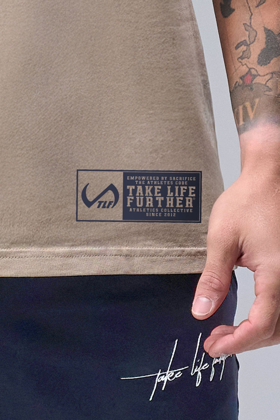 Detail Front View of Tan TLF Property Of Heavy Cotton Muscle Tank featuring a distressed graphic design and raw edge arm holes.