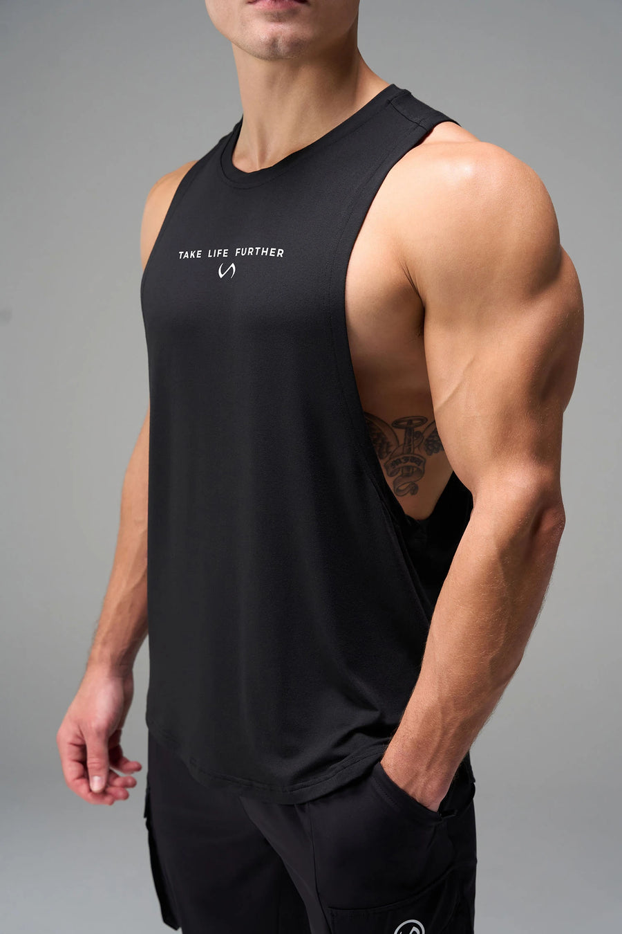 Black Further Air-Flex Drop Arm Tank showing ultra-soft performance fabric and Take Life Further® chest logo detail by TLF Apparel – detail view