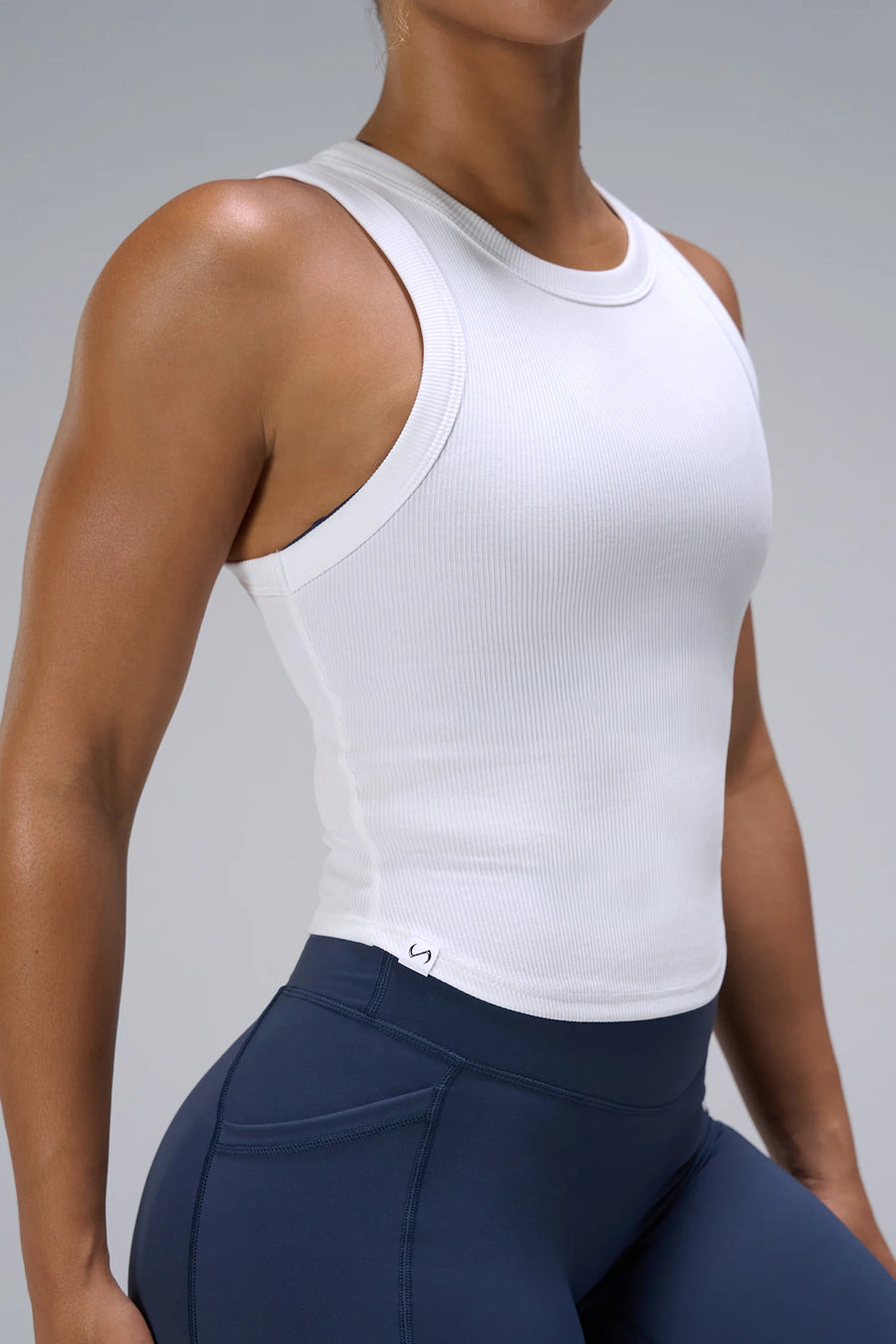 White Essential Ribbed Tank Top showing Hi-Tech Gel icon logo on woven tab at right hem by TLF Apparel – detail view