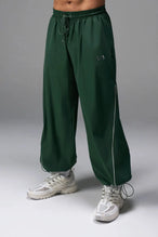 Front View of Green TLF Baggy Track Pants (Men’s GTS Gym-To-Street Edition) featuring side pockets and reflective piping details with an oversized fit 
