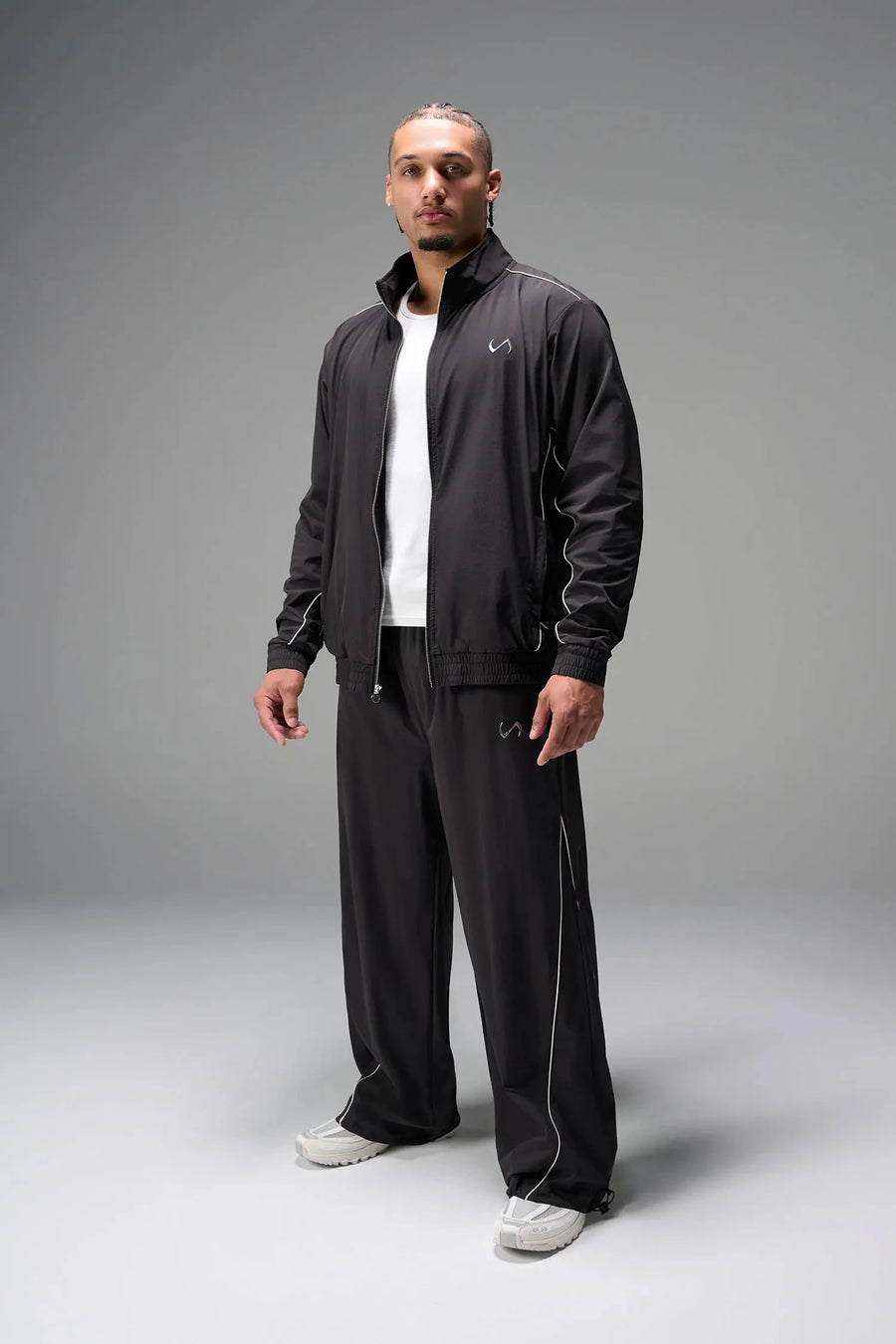 Front View of Black TLF Baggy Track Pants (Men’s GTS Gym-To-Street Edition) featuring side pockets and reflective piping details with an oversized fit 