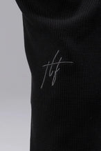 Detail View of Rubber Patch Logo On Left Leg Black TLF GTS Waffle Tech Joggers, featuring an athletic relaxed fit with zipper pockets designed for all day wear