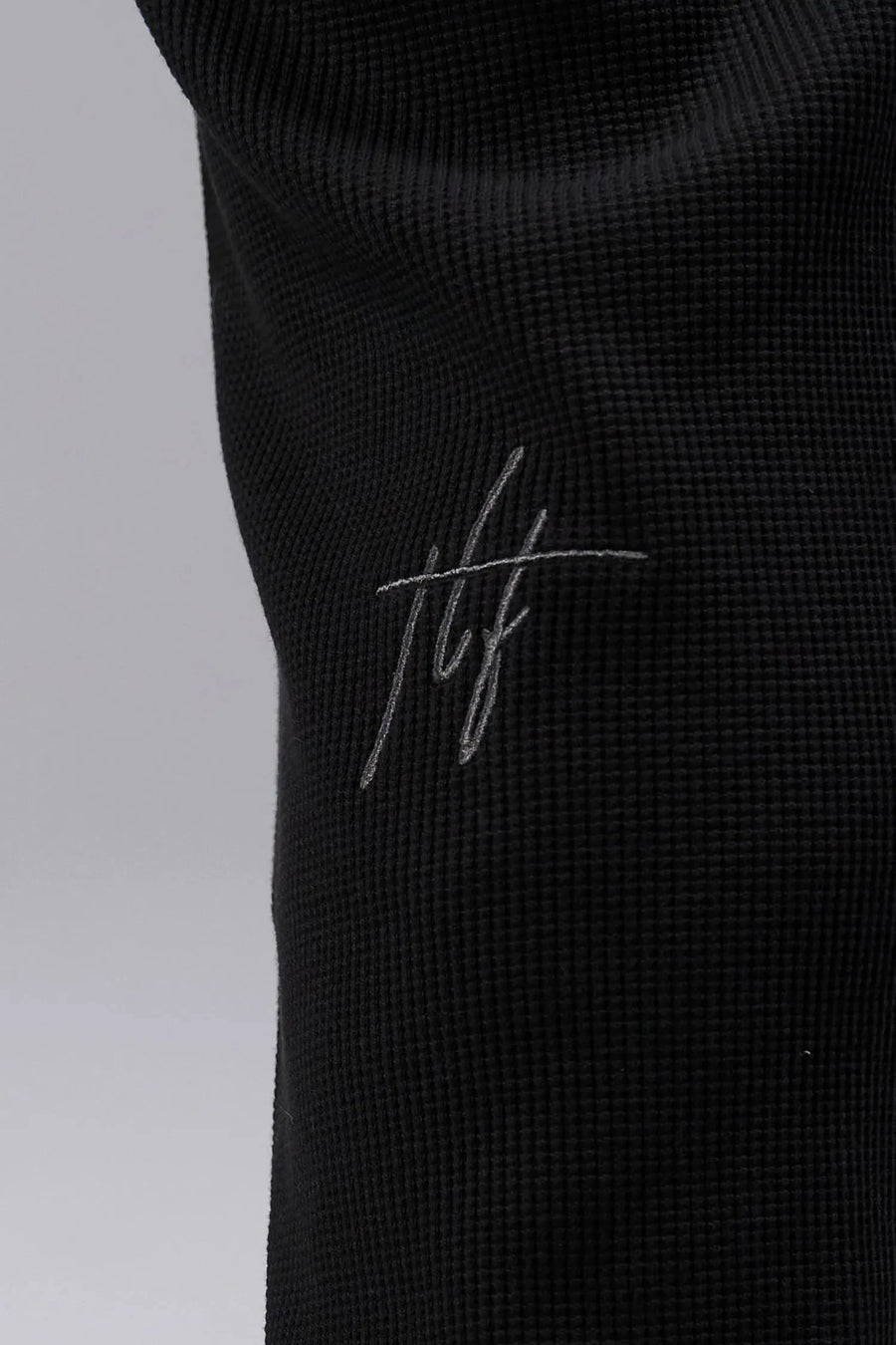 Detail View of Rubber Patch Logo On Left Leg Black TLF GTS Waffle Tech Joggers, featuring an athletic relaxed fit with zipper pockets designed for all day wear