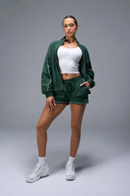 Front View of Green TLF Track Shorts (Women’s GTS Gym-To-Street Edition) featuring side pockets, mesh lining and reflective piping details.