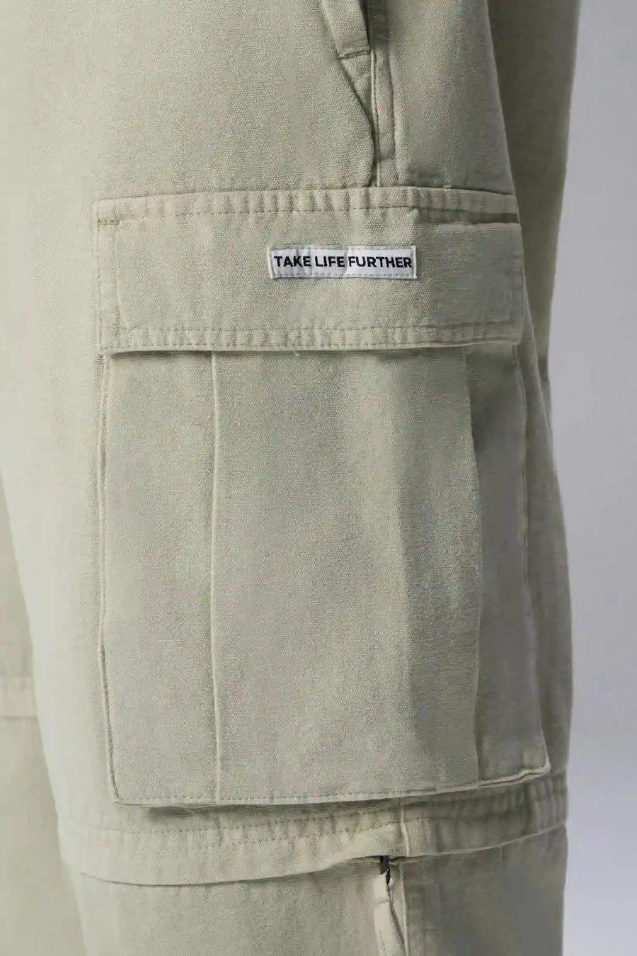 Detail Front View of Green the TLF Zip off cargo pants featuring side cargo pockets and a zip off design that transforms them into shorts