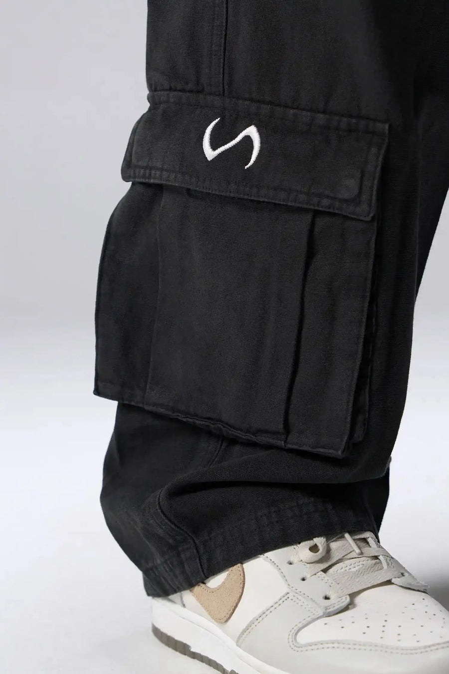Detail View of Black the TLF Zip off cargo pants featuring side cargo pockets and a zip off design that transforms them into shorts